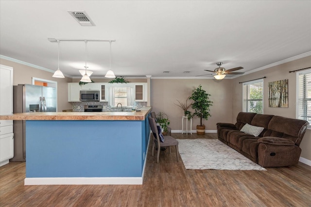 kitchen with appliances with stainless steel finishes, backsplash, track lighting, decorative light fixtures, and white cabinetry