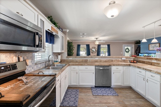 kitchen featuring kitchen peninsula, appliances with stainless steel finishes, sink, decorative light fixtures, and white cabinetry