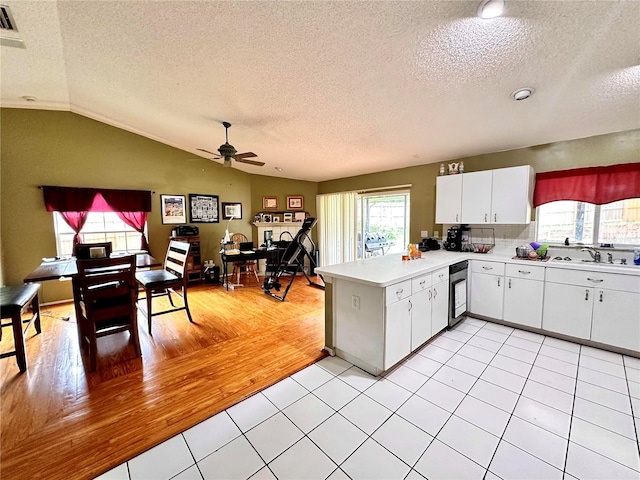 kitchen featuring kitchen peninsula, vaulted ceiling, ceiling fan, light tile patterned flooring, and white cabinetry