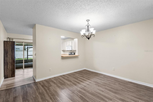 empty room with a notable chandelier, light hardwood / wood-style flooring, and a textured ceiling