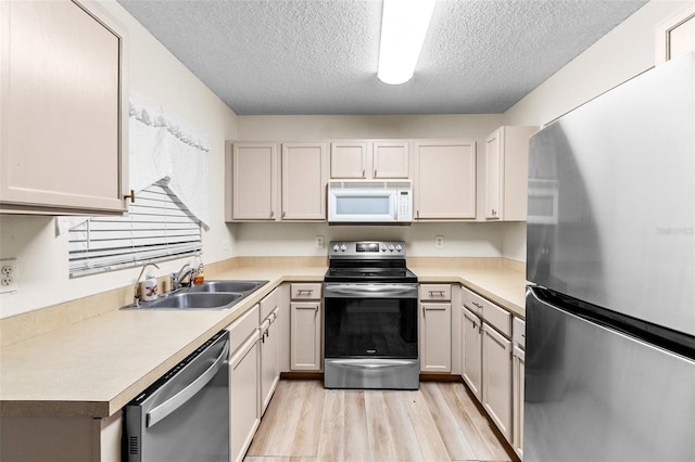 kitchen with a textured ceiling, stainless steel appliances, sink, and light hardwood / wood-style flooring