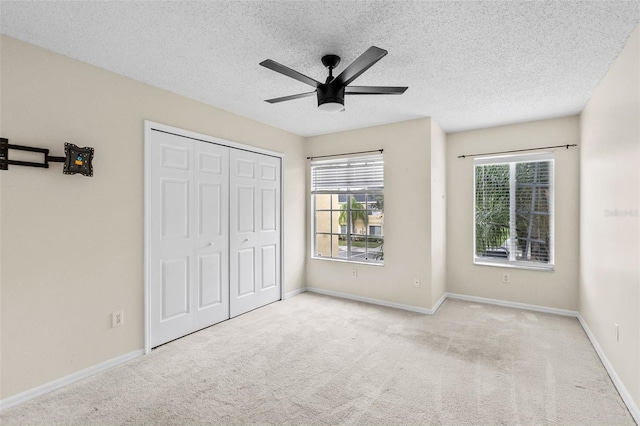 unfurnished bedroom with ceiling fan, light colored carpet, a textured ceiling, and a closet