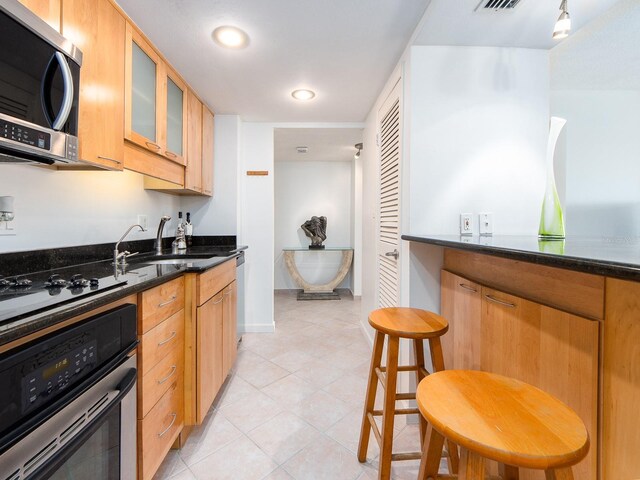 kitchen featuring appliances with stainless steel finishes, sink, light tile patterned floors, and dark stone counters