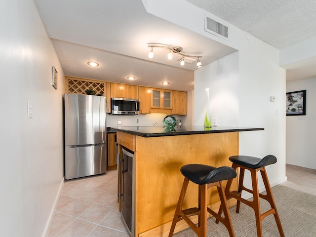 kitchen with light tile patterned flooring, beverage cooler, a kitchen breakfast bar, kitchen peninsula, and stainless steel appliances