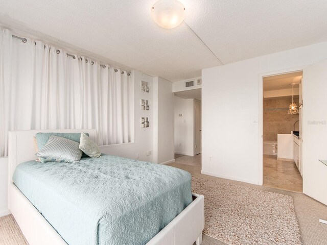 bedroom featuring ensuite bath, light carpet, and a textured ceiling