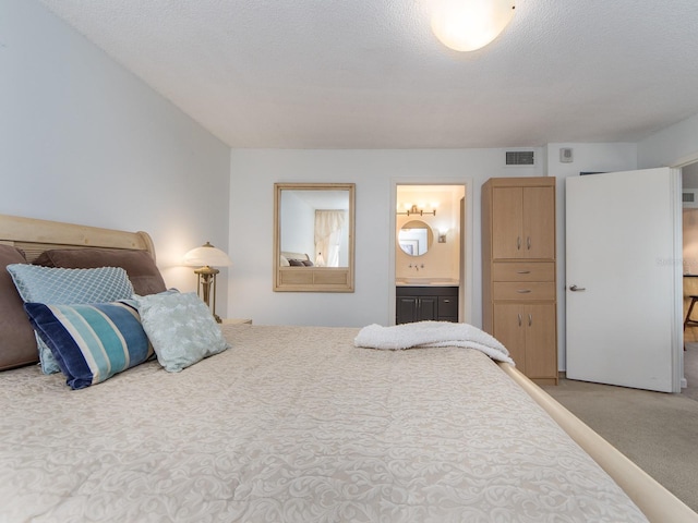 bedroom with ensuite bath, a textured ceiling, and carpet flooring