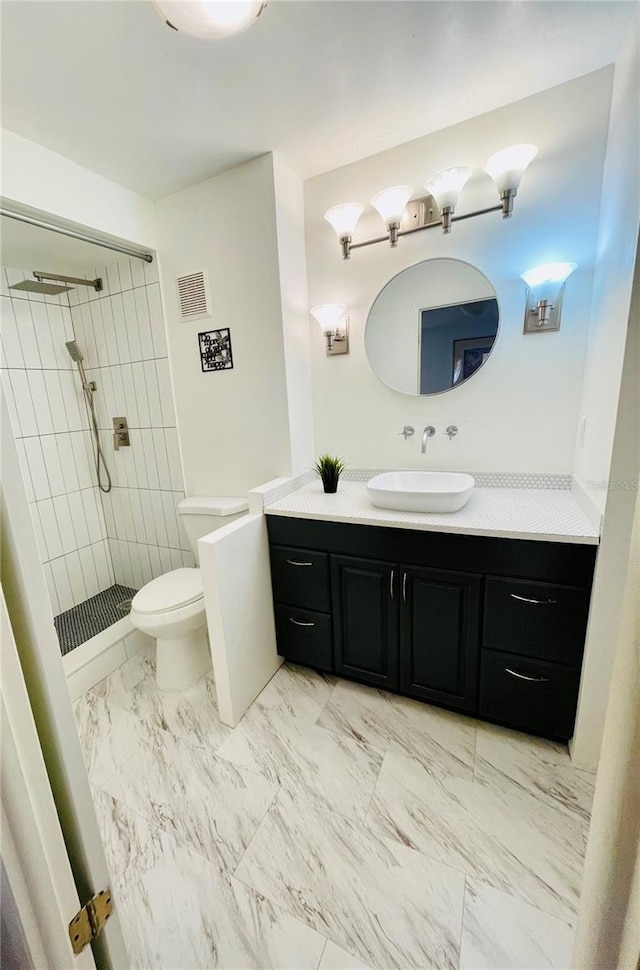 bathroom with vanity, tiled shower, and toilet