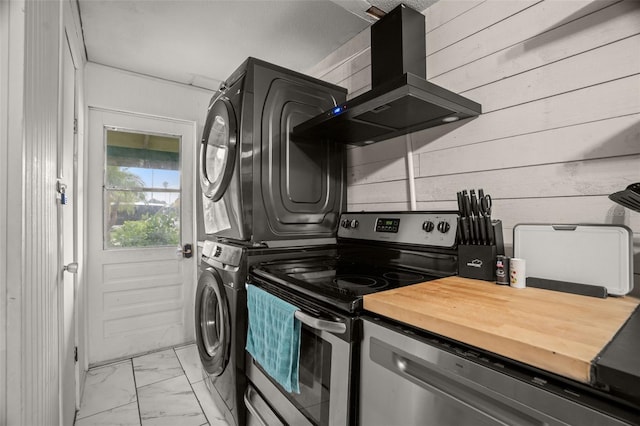 kitchen featuring appliances with stainless steel finishes, stacked washer / drying machine, wooden walls, and range hood