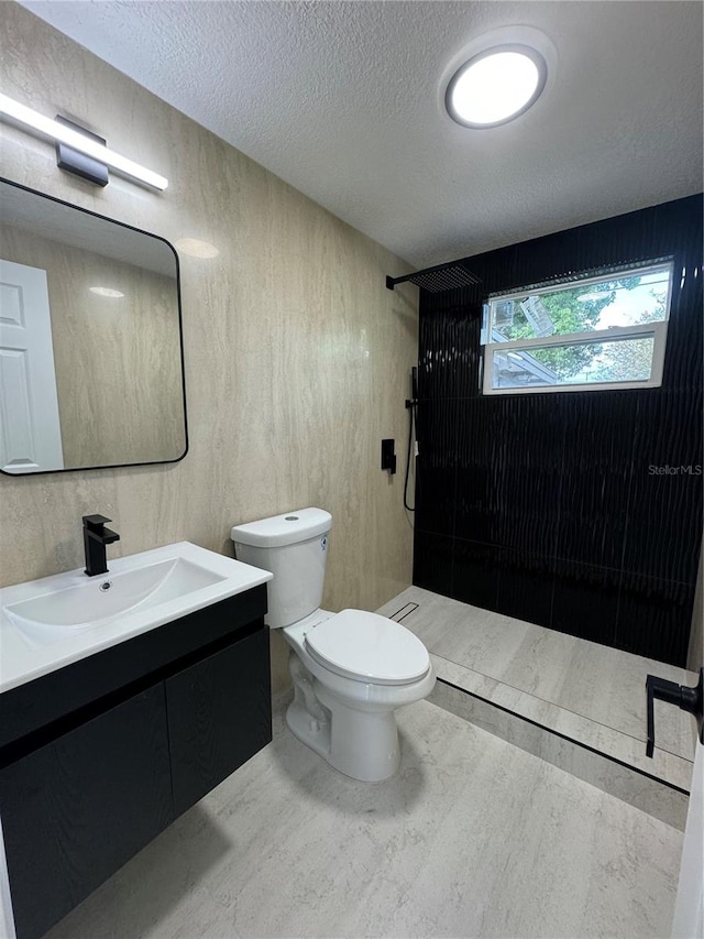 bathroom featuring vanity, toilet, a textured ceiling, and tiled shower