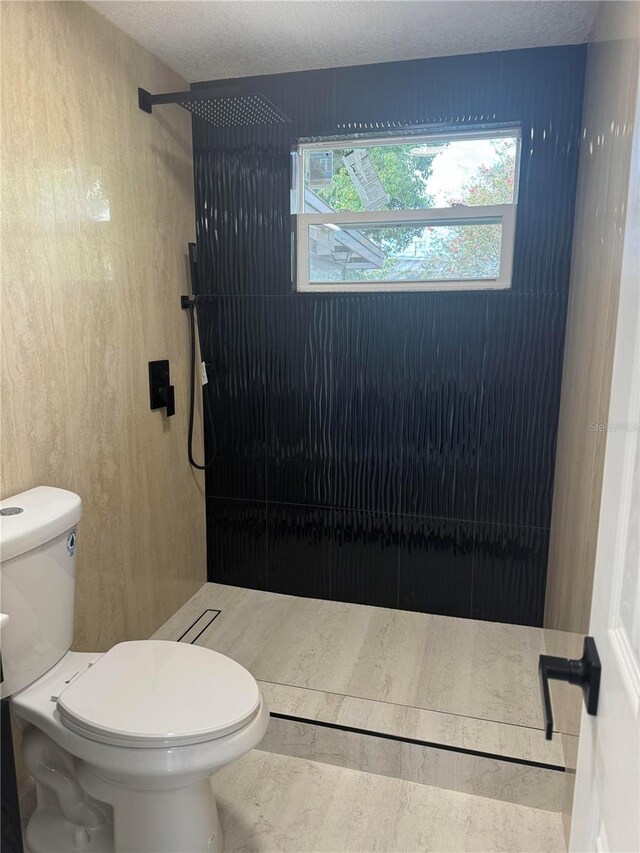 bathroom with a tile shower, a textured ceiling, and toilet