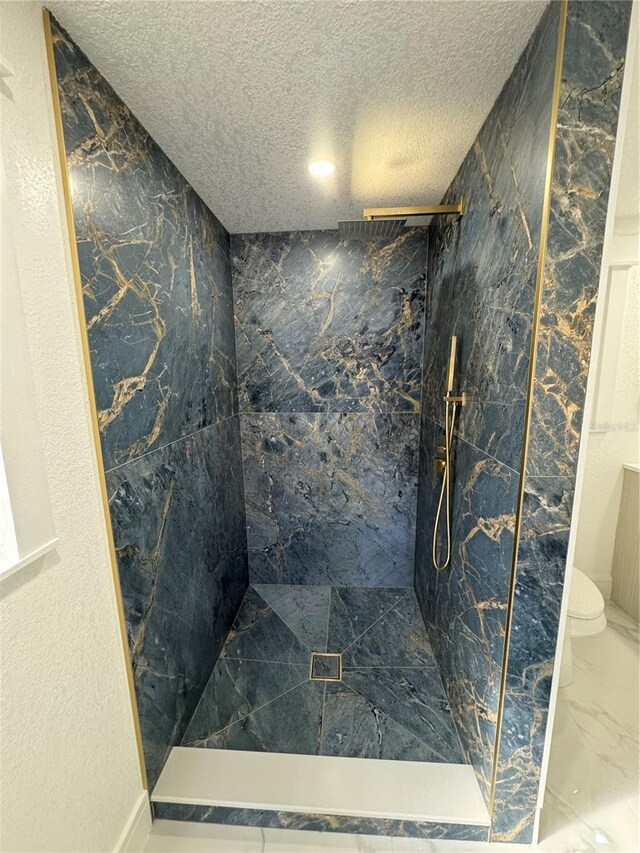 bathroom with a textured ceiling, toilet, and tiled shower