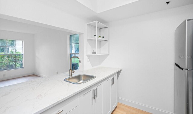 kitchen featuring light wood-type flooring, stainless steel refrigerator, white cabinetry, light stone counters, and sink