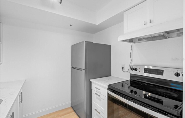 kitchen featuring light wood-type flooring, appliances with stainless steel finishes, light stone counters, and white cabinetry