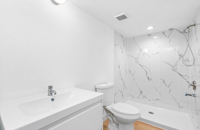 bathroom with vanity, toilet, a tile shower, and hardwood / wood-style floors