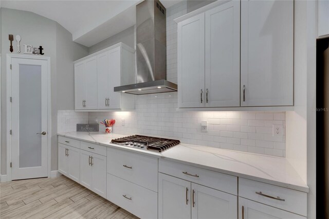 kitchen with wall chimney range hood, stainless steel gas cooktop, light hardwood / wood-style floors, and white cabinetry