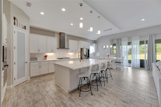 kitchen with decorative light fixtures, light wood-type flooring, white cabinetry, a spacious island, and wall chimney exhaust hood