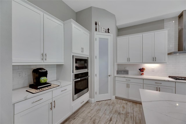 kitchen with white cabinets, backsplash, stainless steel appliances, and light hardwood / wood-style flooring