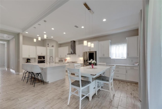 kitchen featuring a spacious island, a kitchen breakfast bar, stainless steel fridge, and wall chimney exhaust hood