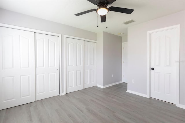 unfurnished bedroom featuring light wood-type flooring, ceiling fan, and multiple closets