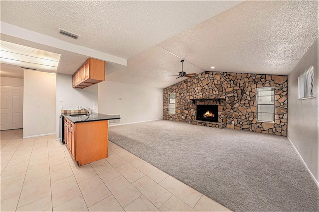 kitchen featuring a stone fireplace, kitchen peninsula, a textured ceiling, ceiling fan, and light carpet