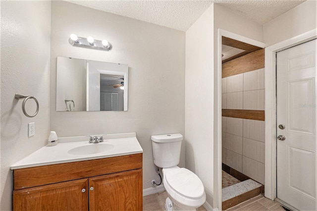 bathroom featuring a textured ceiling, a tile shower, vanity, and toilet