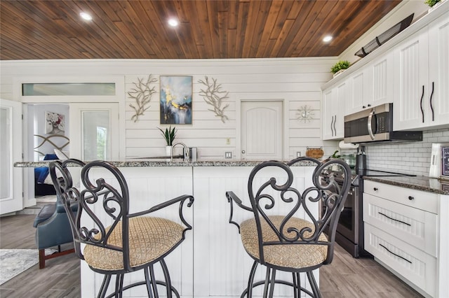 kitchen featuring appliances with stainless steel finishes, dark stone counters, dark wood-type flooring, and white cabinets