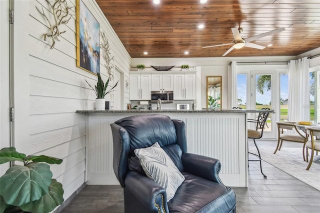 living area featuring ceiling fan, dark hardwood / wood-style floors, wood walls, and wooden ceiling