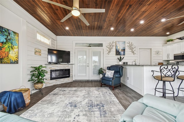 living room featuring wooden ceiling, wooden walls, dark wood-type flooring, and ceiling fan