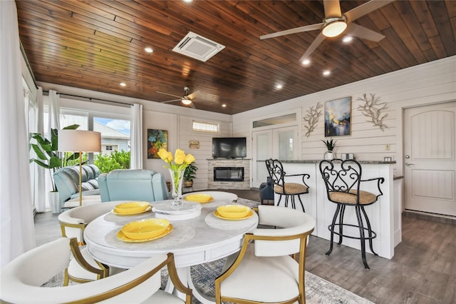 dining area featuring ceiling fan, wooden ceiling, and a stone fireplace