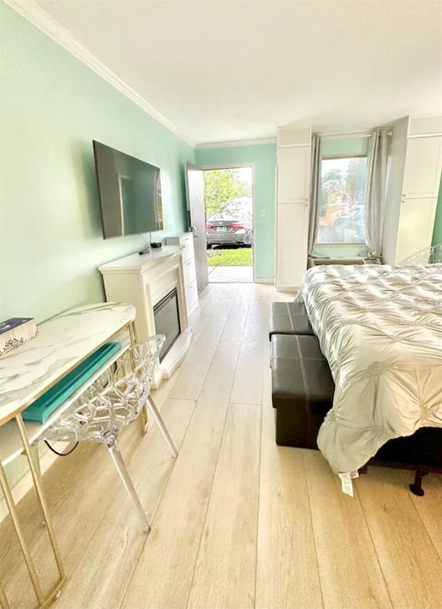 bedroom with light wood-type flooring, a glass covered fireplace, and ornamental molding