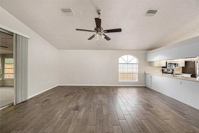 unfurnished living room with ceiling fan, a textured ceiling, dark wood-type flooring, and a healthy amount of sunlight