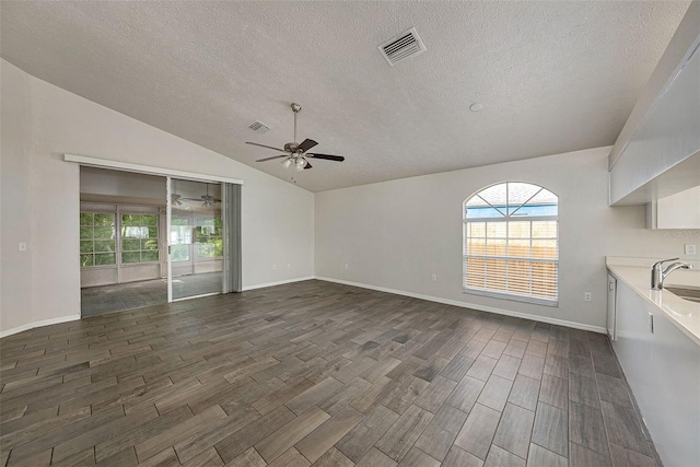 unfurnished living room featuring ceiling fan, vaulted ceiling, a textured ceiling, and dark hardwood / wood-style flooring