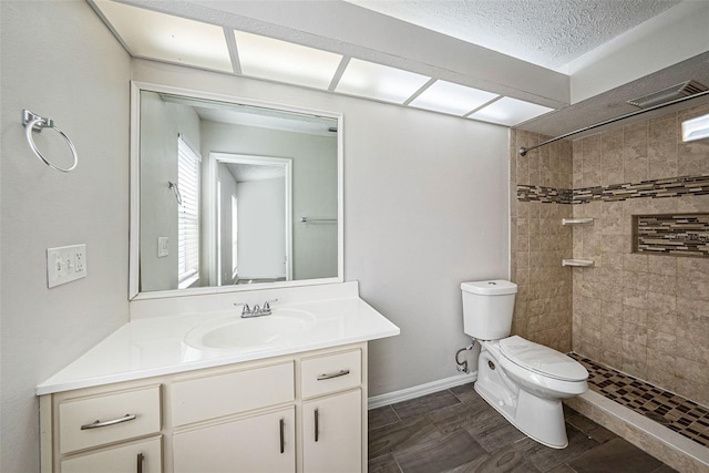 bathroom with a textured ceiling, a tile shower, vanity, and toilet