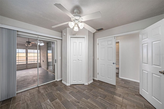 unfurnished bedroom with a textured ceiling, dark hardwood / wood-style flooring, ceiling fan, and a closet