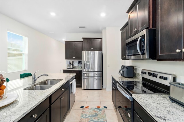 kitchen featuring dark brown cabinets, light tile patterned floors, sink, light stone countertops, and appliances with stainless steel finishes