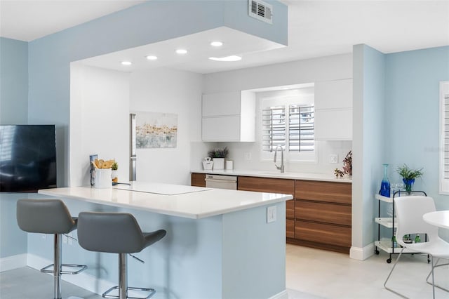 kitchen with a kitchen bar, kitchen peninsula, stainless steel dishwasher, sink, and white cabinetry