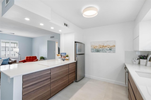 kitchen with white cabinetry, sink, kitchen peninsula, stainless steel fridge, and light tile patterned flooring