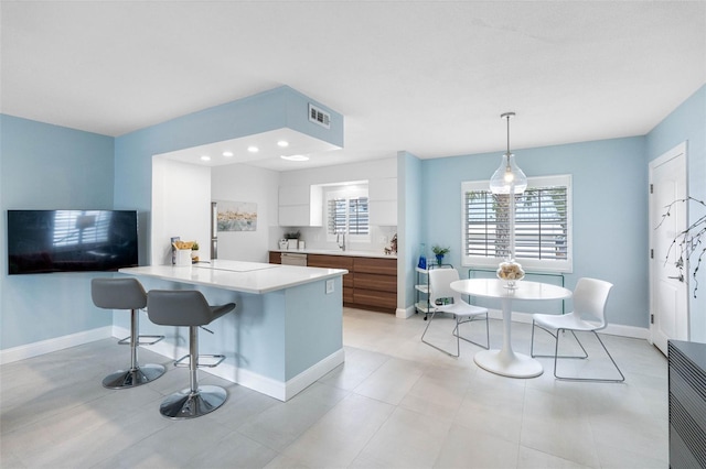 kitchen featuring a center island, white cabinets, sink, decorative light fixtures, and a kitchen bar