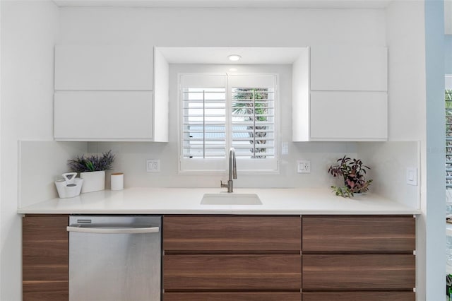 kitchen with a sink, white cabinets, light countertops, stainless steel dishwasher, and modern cabinets