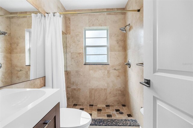 full bathroom with tiled shower, vanity, and toilet