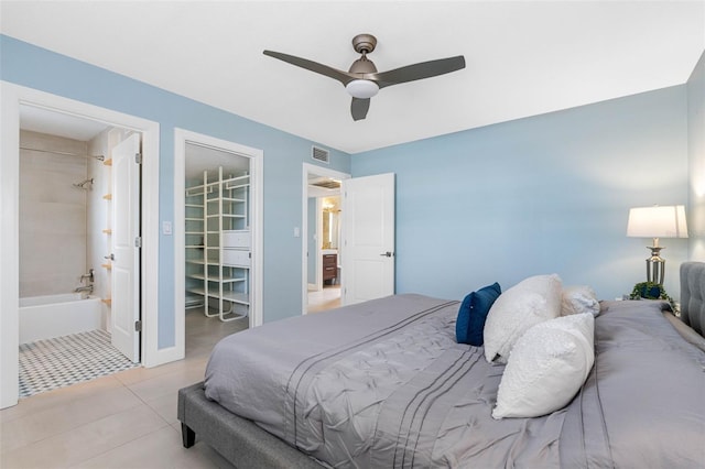 bedroom with a walk in closet, light tile patterned floors, visible vents, a ceiling fan, and connected bathroom