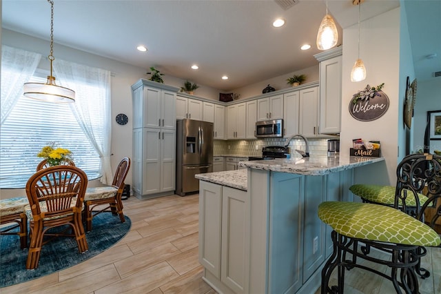 kitchen with light stone countertops, appliances with stainless steel finishes, light hardwood / wood-style floors, kitchen peninsula, and pendant lighting