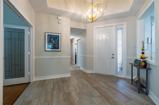 foyer with a tray ceiling, light hardwood / wood-style flooring, and a chandelier