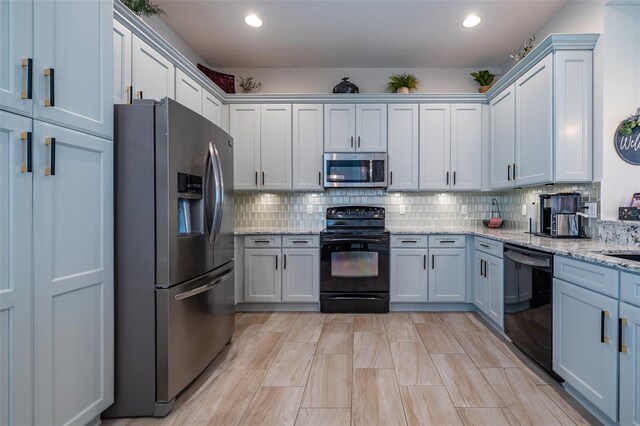 kitchen with black appliances, light stone counters, and backsplash