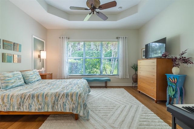 bedroom featuring ceiling fan, dark hardwood / wood-style floors, and a tray ceiling