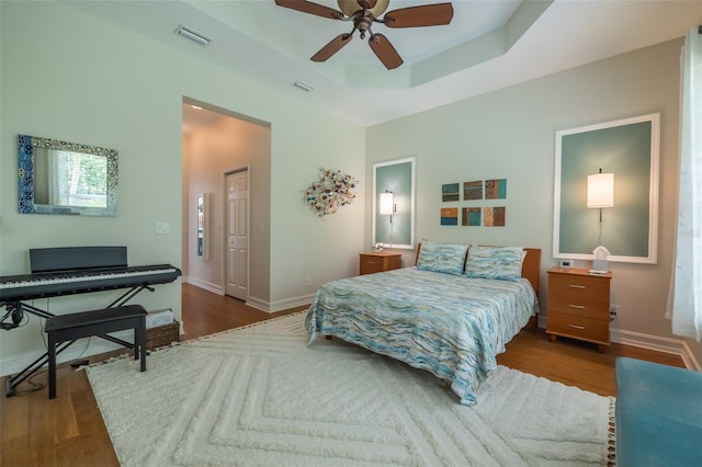 bedroom featuring ceiling fan, dark hardwood / wood-style floors, and a tray ceiling