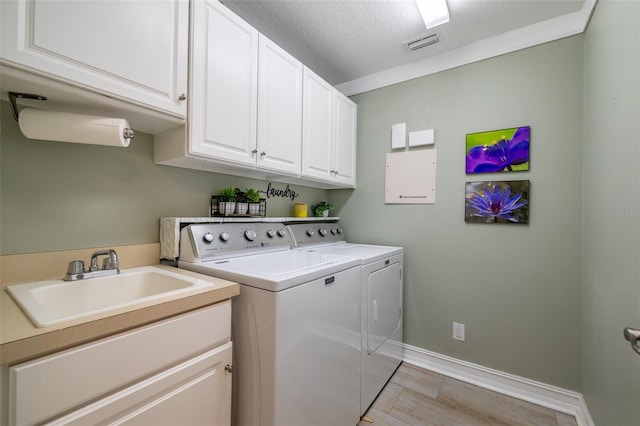 clothes washing area featuring light hardwood / wood-style floors, sink, separate washer and dryer, cabinets, and a textured ceiling