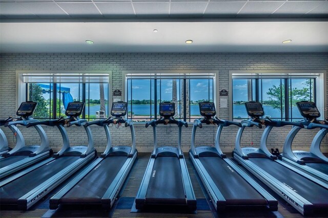 gym featuring a drop ceiling and brick wall