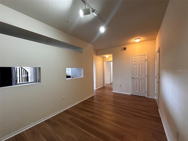 empty room with a textured ceiling, dark wood-type flooring, and rail lighting