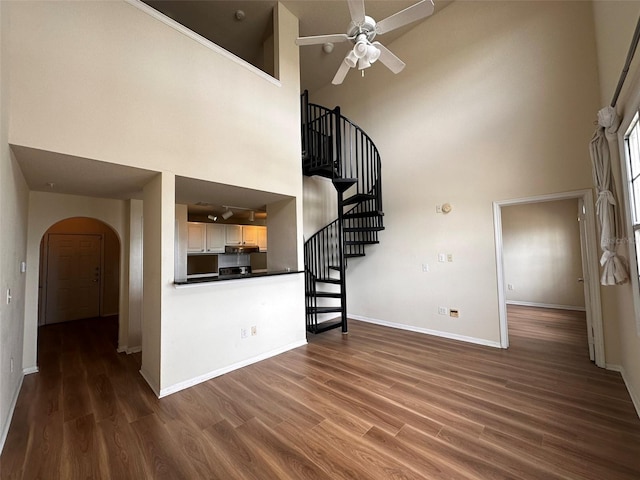 unfurnished living room featuring a high ceiling, dark hardwood / wood-style flooring, and ceiling fan